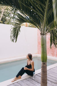 Side view of woman sitting on the floor by the poolside looking up 
