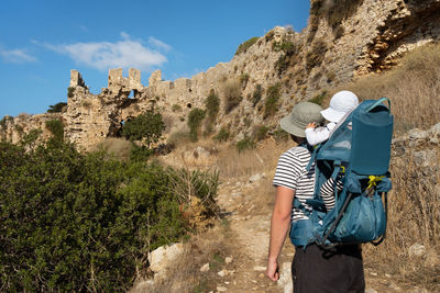 Man with baby carrier travelling, hiking, looking at old fortress 