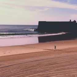 Silhouette person running at beach against sky