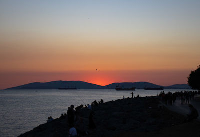 Silhouette people on beach against sky during sunset