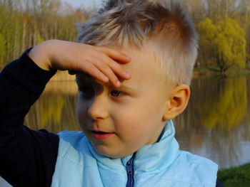 Cute boy shielding eyes against lake