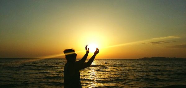 Optical illusion of silhouette man holding sun at beach