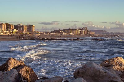 Scenic view of sea by city against sky during sunset