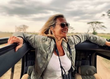 Smiling woman wearing sunglasses while standing by car hood against sky