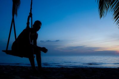 Silhouette of swing at beach against sky during sunset