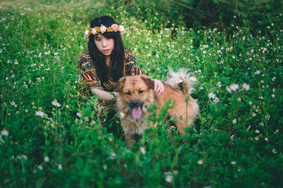 Woman wearing flowers while sitting with dog on field 