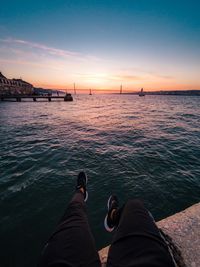 Low section of man sitting on pier over sea against sky during sunset