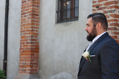 Side view of groom standing against wall