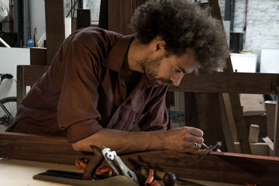 Carpenter measuring wooden plank at workshop