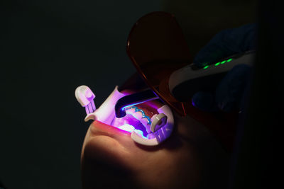 Close-up of hand holding illuminated lighting equipment against black background