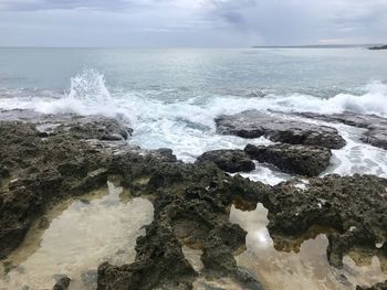 Waves splashing on rocks at shore against sky