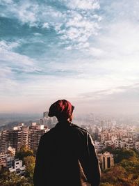 Rear view of man looking at city buildings against sky