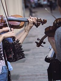 Midsection of people playing violin on street in city
