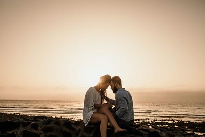 Couple sitting on rock at beach during sunset