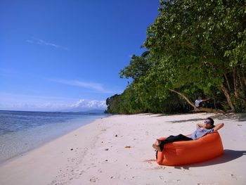 Man sitting on beach by sea against sky