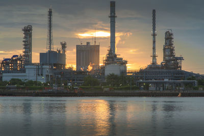 River by illuminated buildings against sky during sunset