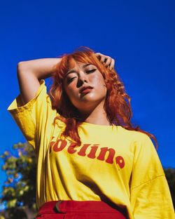 Low angle view of young woman standing against clear blue sky