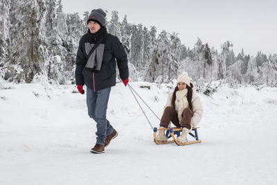 A young guy rides a girl on a sleigh in the forest.