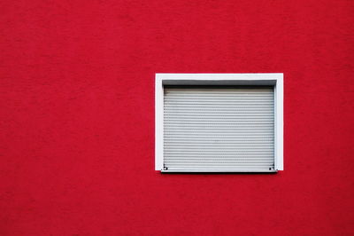 Low angle view of closed window amidst red wall