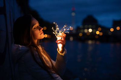 Young woman holding illuminated string light at night