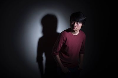 Thoughtful man looking away while standing against wall in darkroom