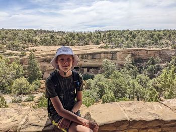 Portrait of teen boy sitting on rocks overlooking mesa verde cliff dwellings