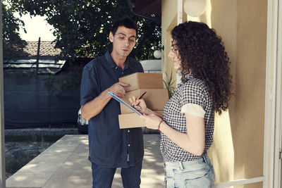 Woman signing on digital tablet while delivery man pointing against house