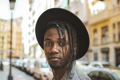 Close-up portrait of young man with braided hair wearing hat in city
