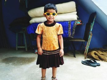 Portrait of young woman wearing sunglasses while standing against wall