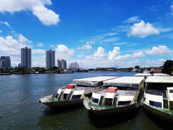 Boats moored in river by city against sky