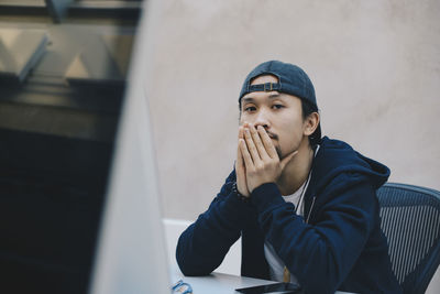 Portrait of young man looking away while sitting on table