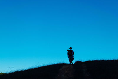 Rear view of man walking on field against clear blue sky