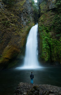 Rear view of man looking at waterfall in forest