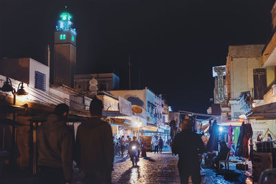 People on illuminated street amidst buildings at night