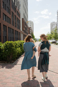 Full length of caucasian mothers carrying their babies in slings on sunny day