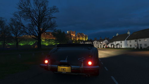 Car on road by illuminated buildings against sky at night