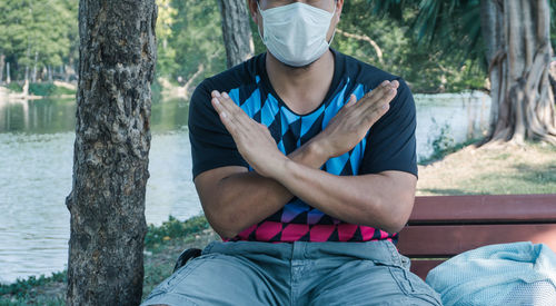 Midsection of man sitting by tree trunk