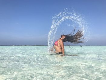 Side view of woman tossing hair while standing in sea against clear sky