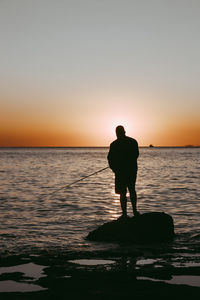 Silhouette man looking at sea against sky during sunset