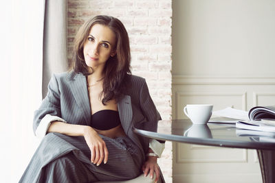 Ballerina in a suit with a cup of coffee smiling and dreaming is sitting at a table by the window