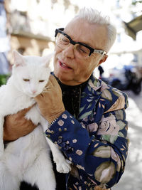 Elderly male in trendy clothes and eyeglasses standing on street with cute fluffy cat