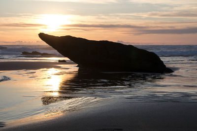 Silhouette rock on beach against sky during sunset