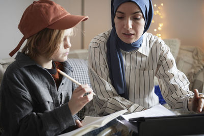 Mother wearing hijab helping son doing homework