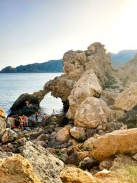 People on rocks by sea against clear sky