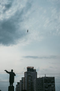 Low angle view of silhouette person standing by buildings against sky