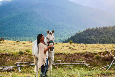 Side view of young woman with horse on field