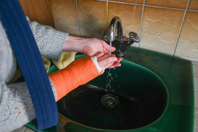 Woman washes her right hand, which is in a cast, under running water with her left hand, washing off