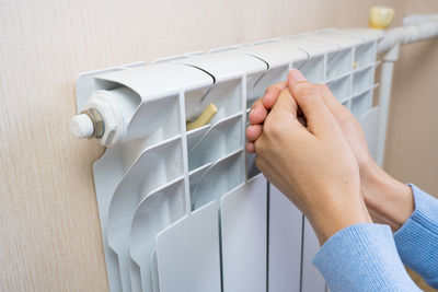 A female warms hands over a battery, a heater at home in a room. 