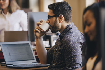 Mid adult businessman drinking coffee with laptop on desk in office