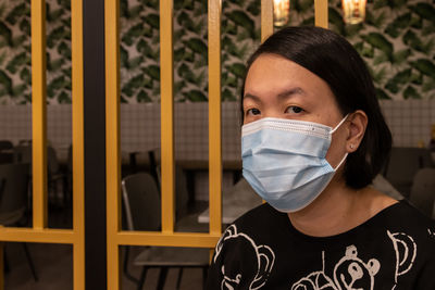 Portrait of woman wearing mask standing by gate